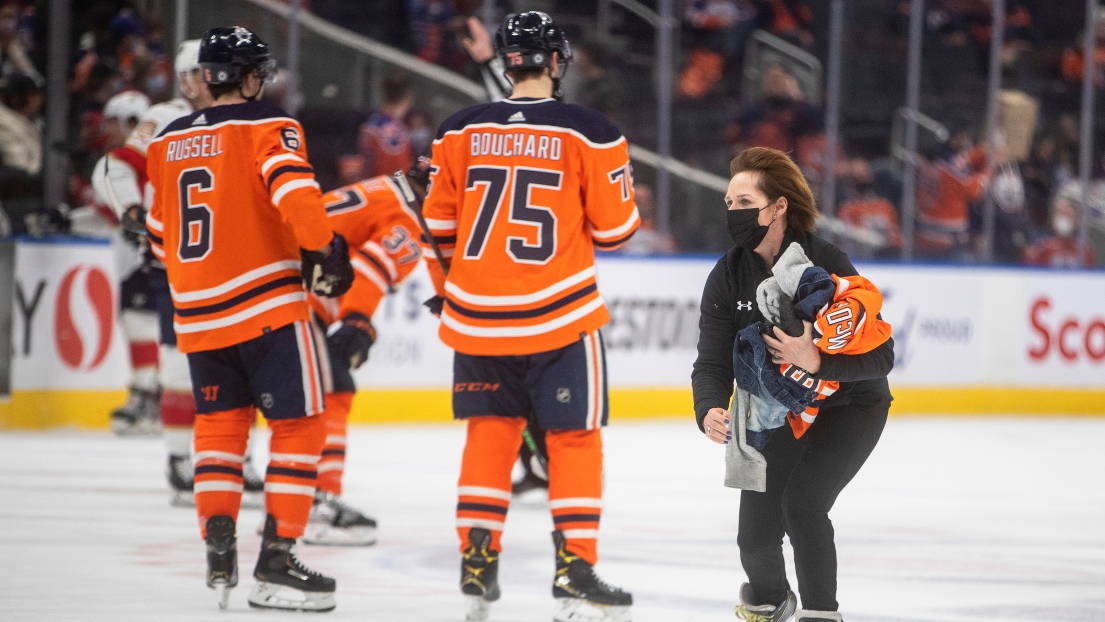 Une préposée ramasse des chandails des Oilers rejetés sur la patinoire à Edmonton